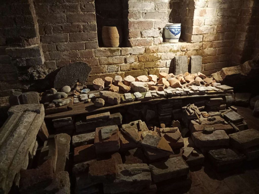 Middeleeuwse kelder, waar verschillende oude stenen en restanten van potten te zien zijn.