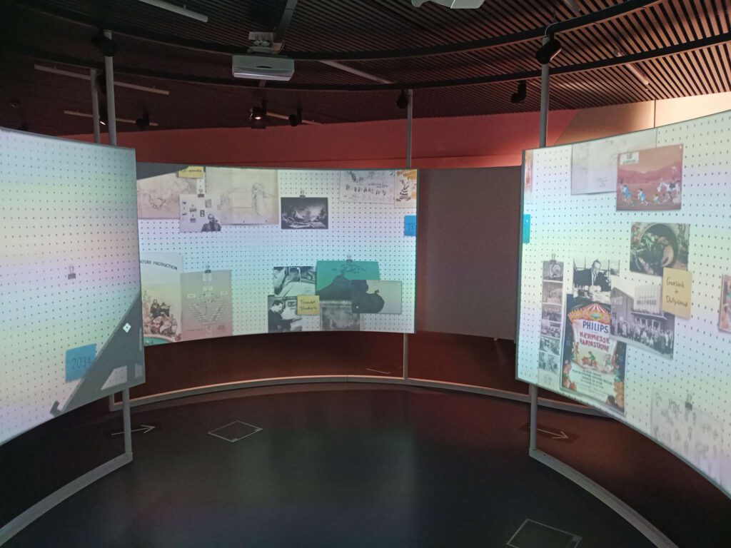 Op de foto staan 3 halfronde projectieschermen met daarop een animatie van het museum. Daarboven hangen speakers die geluid produceren.