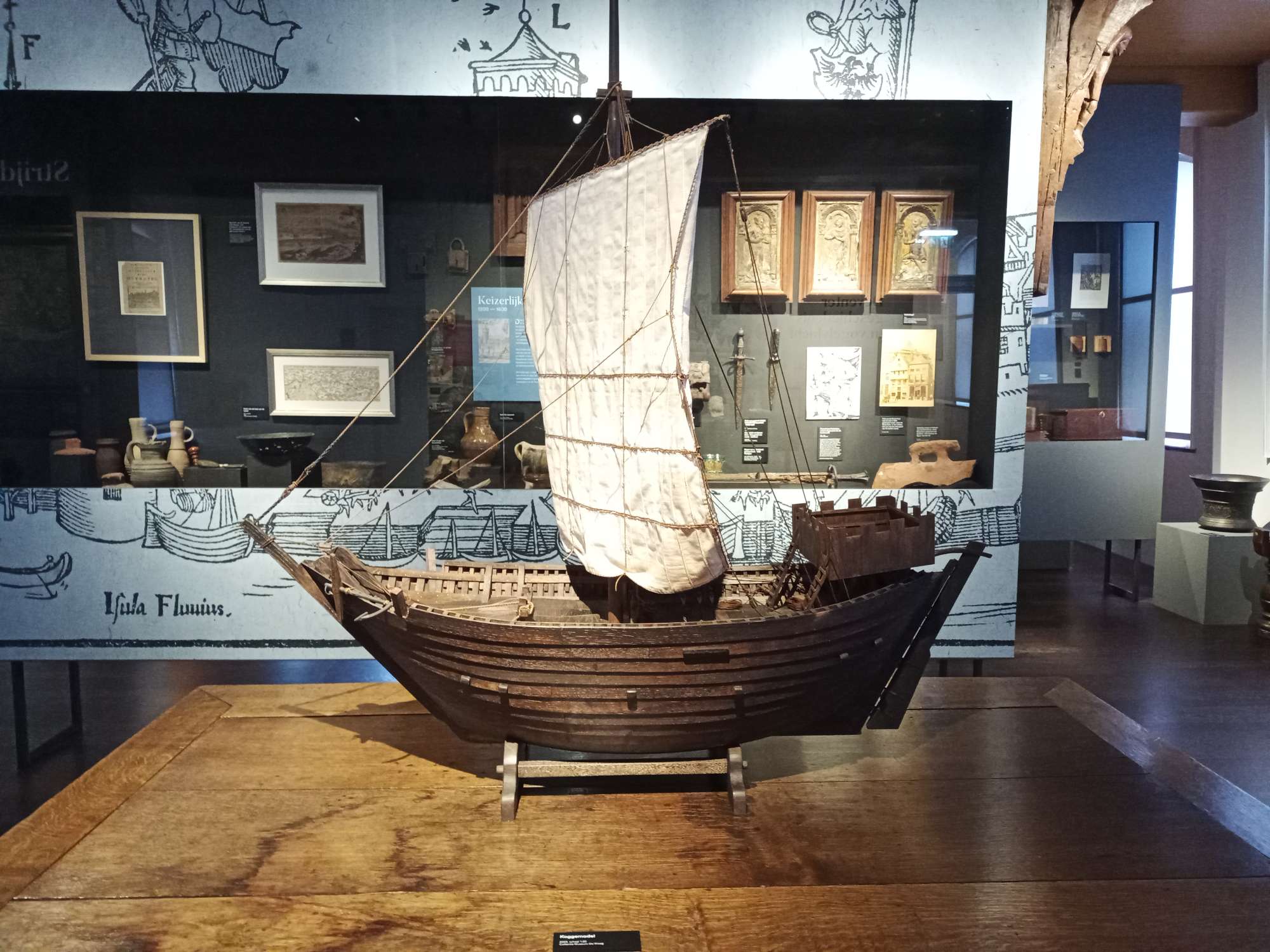Een houten modelschip met een wit zeil.