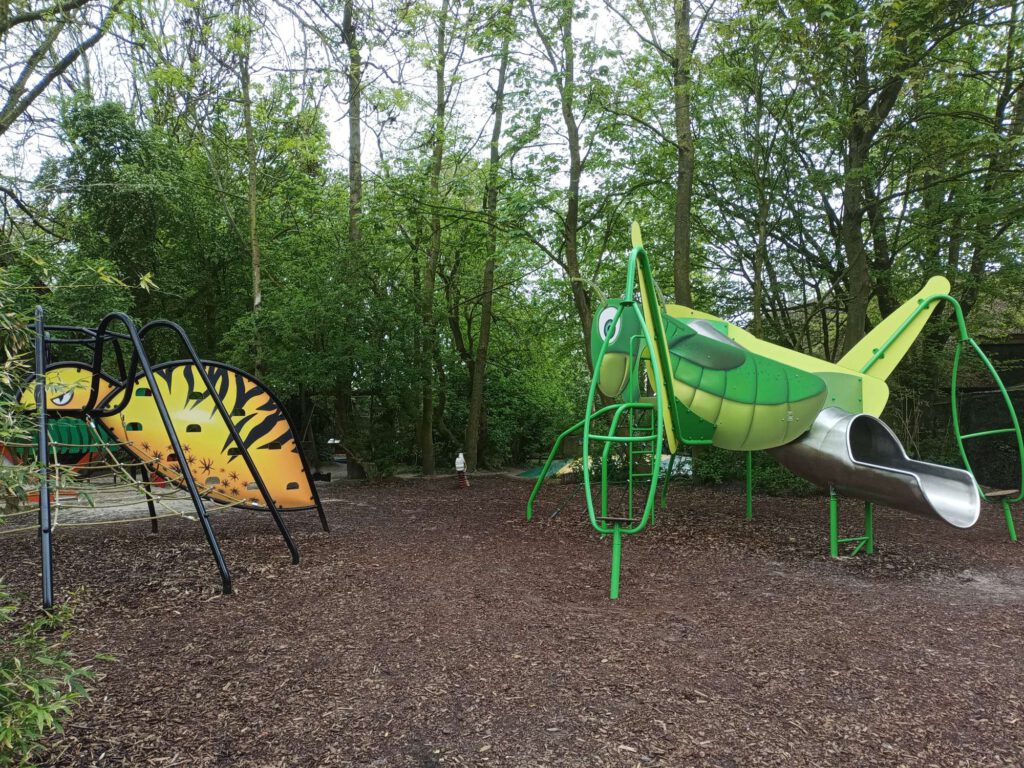 Een speeltuin die vormgegeven is als grote insecten, zoals een bij en een sprinkhaan op deze foto.