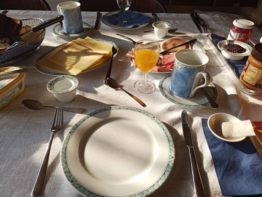Een ontbijttafel bij Bed and breakfast Sinke, met daarop onder andere glaasje sap, kaasplakken, boter, diverse vleeswaren en uiteraard een eierdophouder, bestek en een bord.